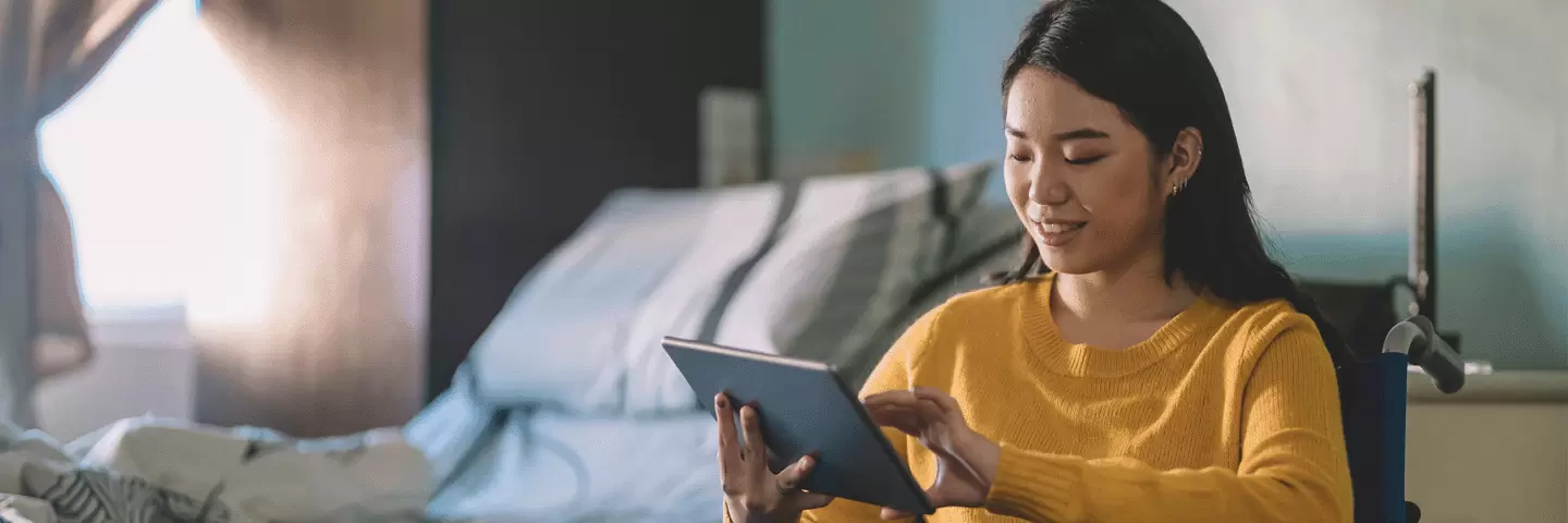 Eine junge Frau im Rollstuhl hält ein Tablet in der Hand.