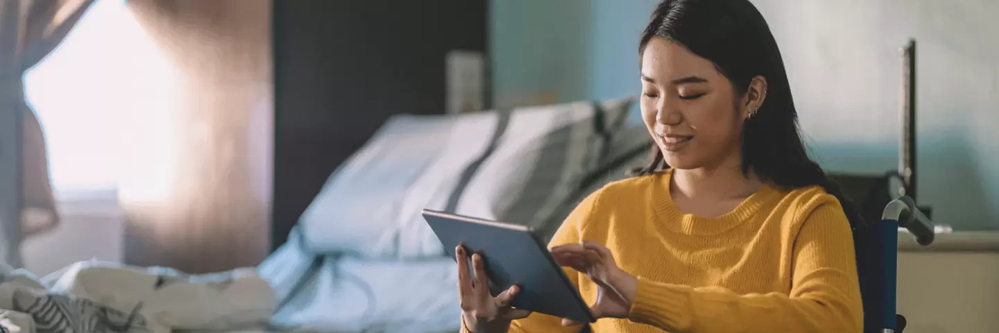 Eine junge Frau im Rollstuhl hält ein Tablet in der Hand.