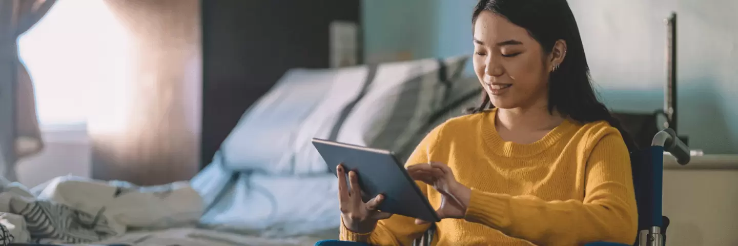 Eine junge Frau im Rollstuhl hält ein Tablet in der Hand.