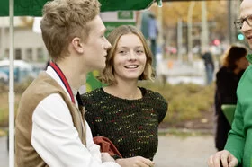 Ein AOK-Mitarbeiter unterhält sich draußen an einem Stand mit einem Jungen und einem Mädchen. 