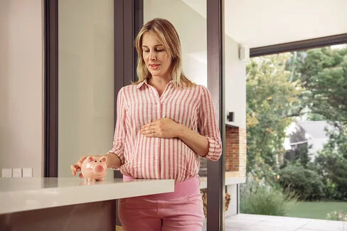 Eine schwangere Frau nimmt ein Sparschwein in die Hand. Die AOK unterstützt Frauen finanziell mit dem Mutterschaftsgeld. 