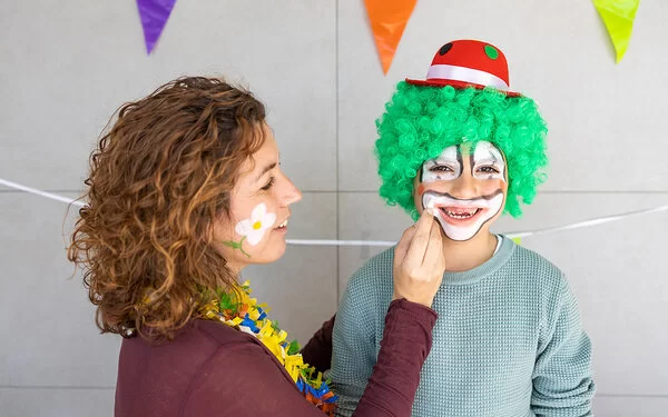 Eine Frau schminkt das Gesicht eines Kindes wie bei einem Clown.