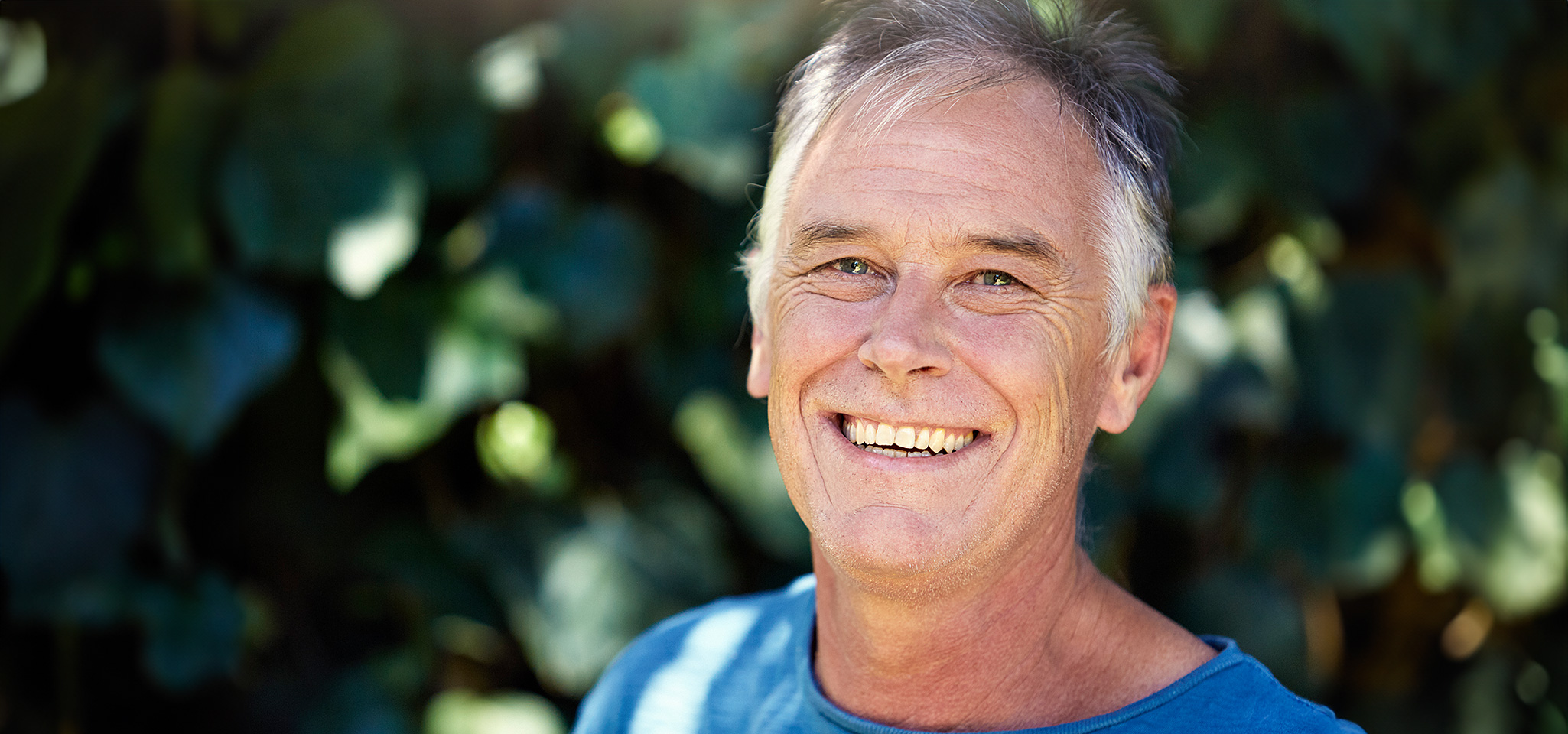 Brustbild eines etwa 60-jährigen Mannes, der freundlich lächelt. Dabei zeigen sich deutlich Mimikfalten auf den Wangen und um die Augen.