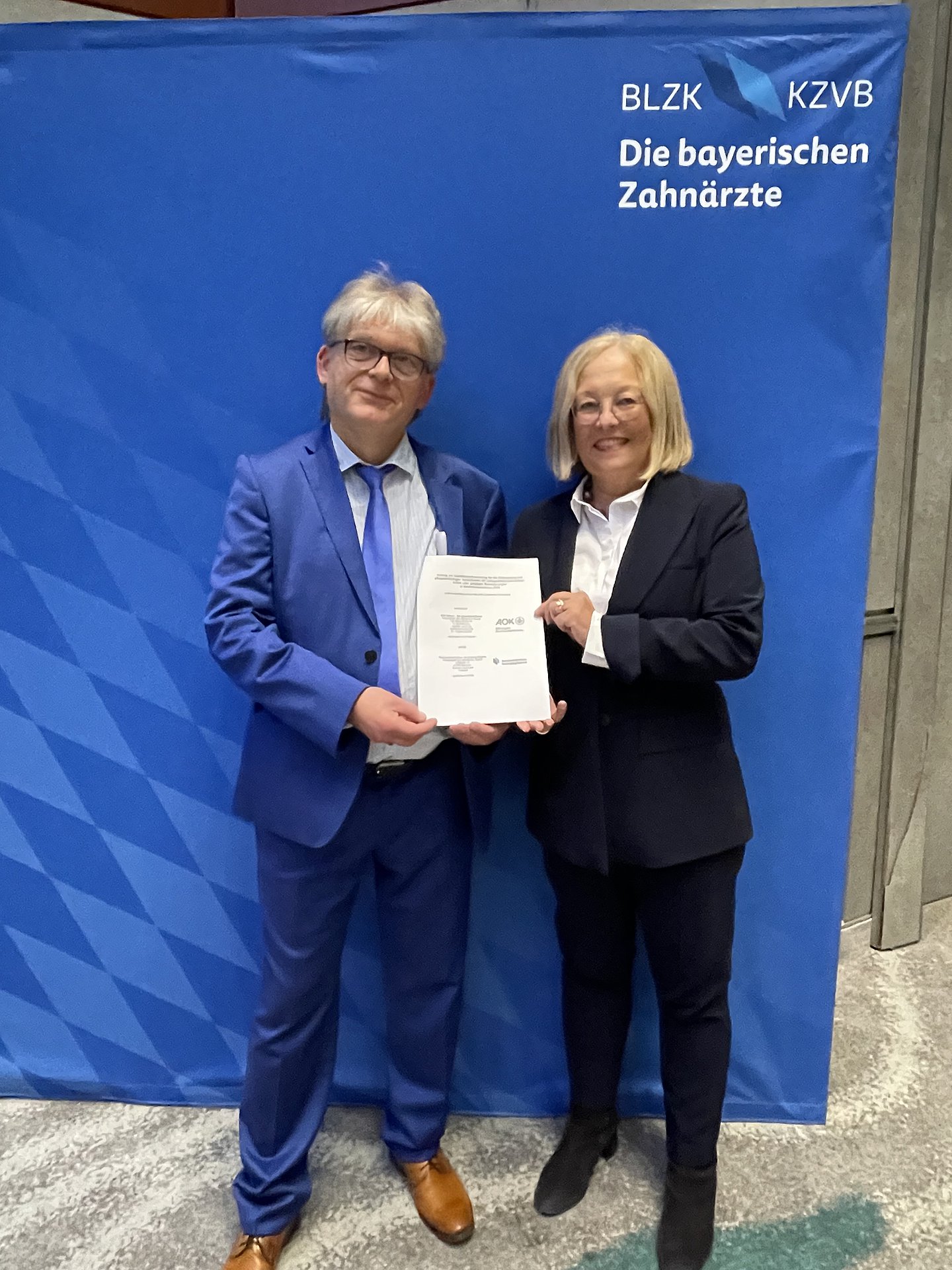 Foto zeigt Dr. Rüdiger Schott, Vorsitzender des Vorstands der KZVB, und Dr. Irmgard Stippler, Vorstandsvorsitzende der AOK Bayern, die einen Vertrag unterzeichneten, der die zahnmedizinische Versorgung von Pflegebedürftigen mit schwerwiegenden körperlichen oder geistigen Behinderungen verbessert. 