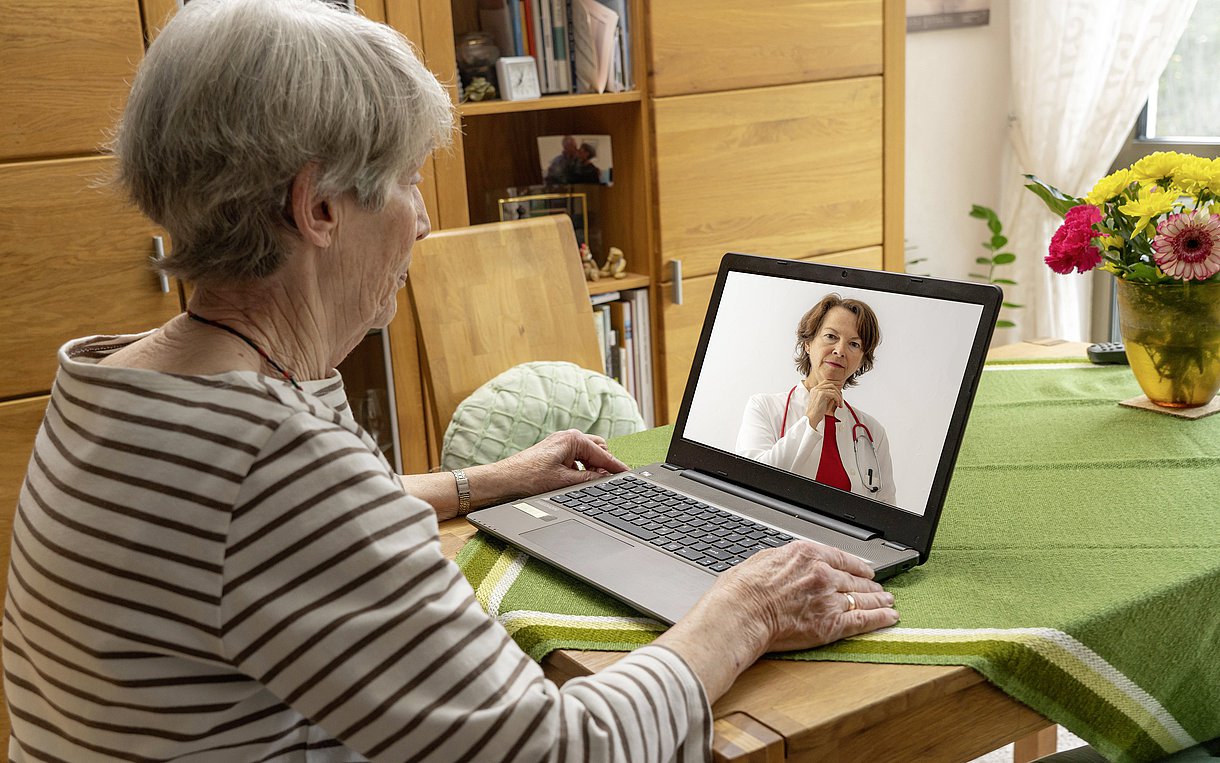 Foto: Eine ältere Dame ist bei einer Videosprechstunde zu Hause am Laptop.