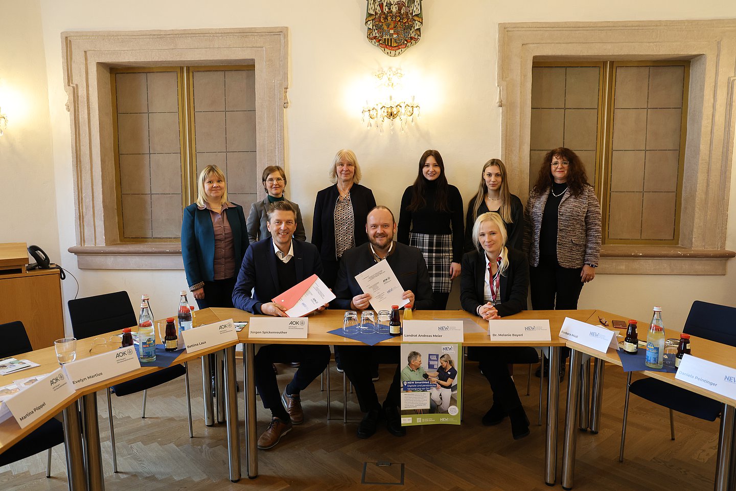 Gruppenfoto mit im Bild von links sitzend: Jürgen Spickenreuther (Direktor der AOK Nordoberpfalz), Andreas Meier (Landrat des Landkreises Neustadt an der Waldnaab NEW), Dr. Melanie Bayerlein (stv. Abteilungsleiterin Gesundheitsamt NEW). Im Bild von links stehend: aus dem Fachbereich "Strategie und Verträge, Versorgungsmanagement der AOK Bayern" Evelyn Martius (Teamleiterin) mit Martina Pöppel (Referentin) und Bettina Laux (Fachbereichsleiterin) sowie als Projektverantwortliche im Landkreis NEW Daniela Peintinger (Gesundheitsamt), Emilia Stauner (Landratsamt) und Barbara Mädl (Landratsamt)