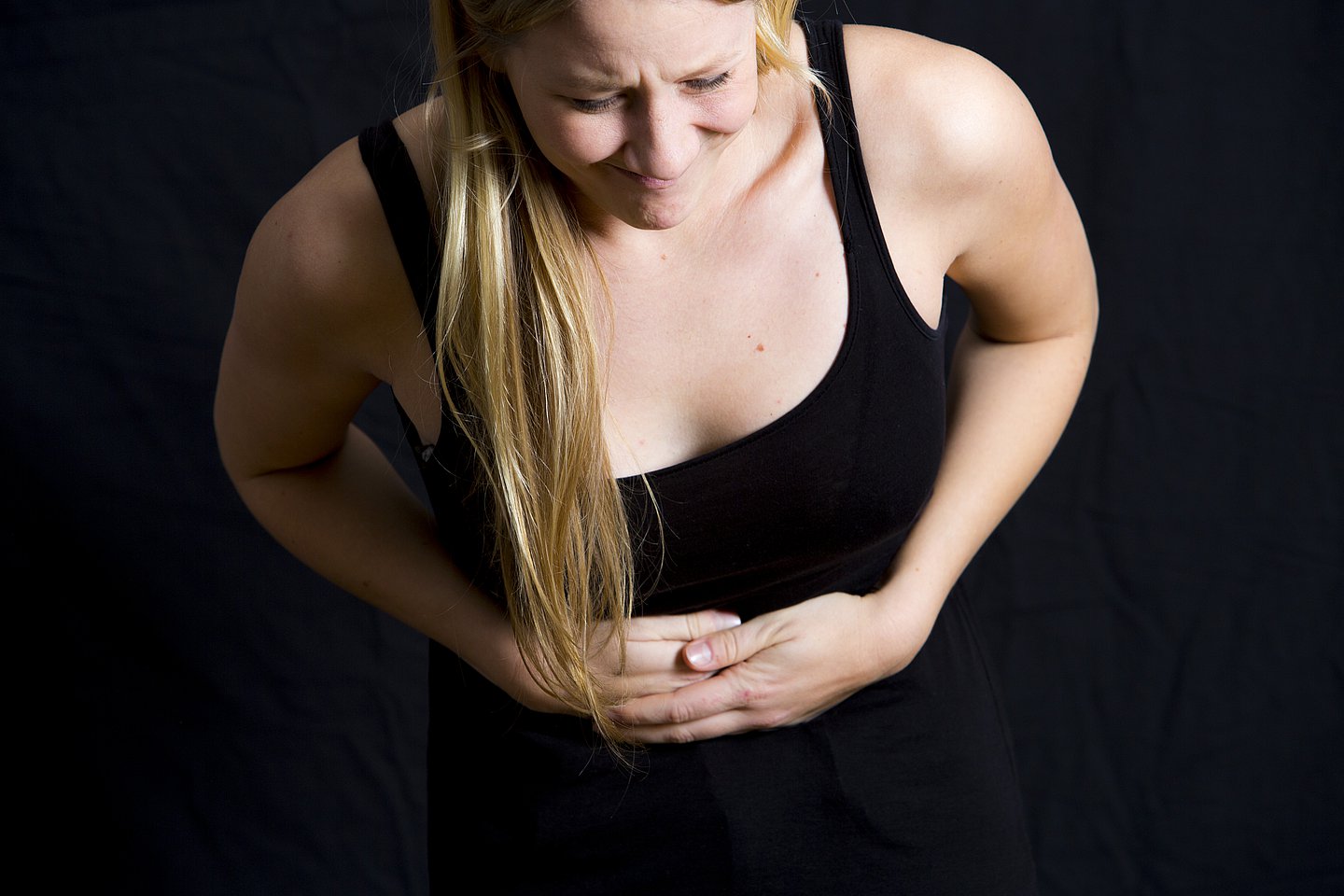 Foto: Eine Frau fasst sich verkrampft an den Bauch.