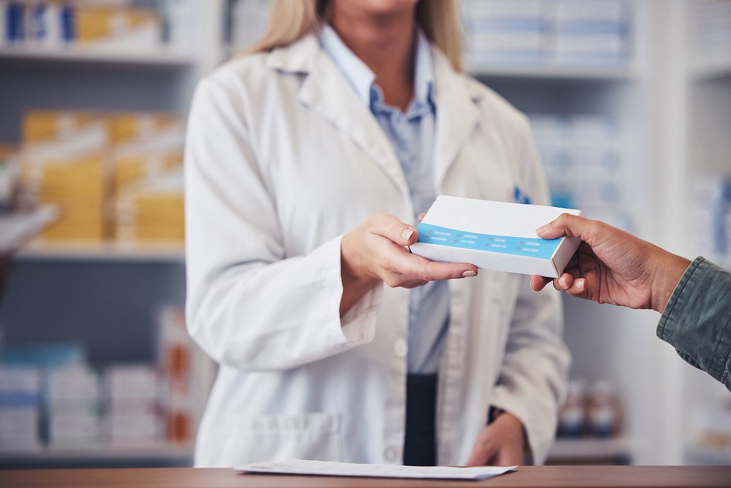 In einer Apotheke reicht eine Apothekerin einem Kunden eine Packung mit Medikamenten über den Tresen.