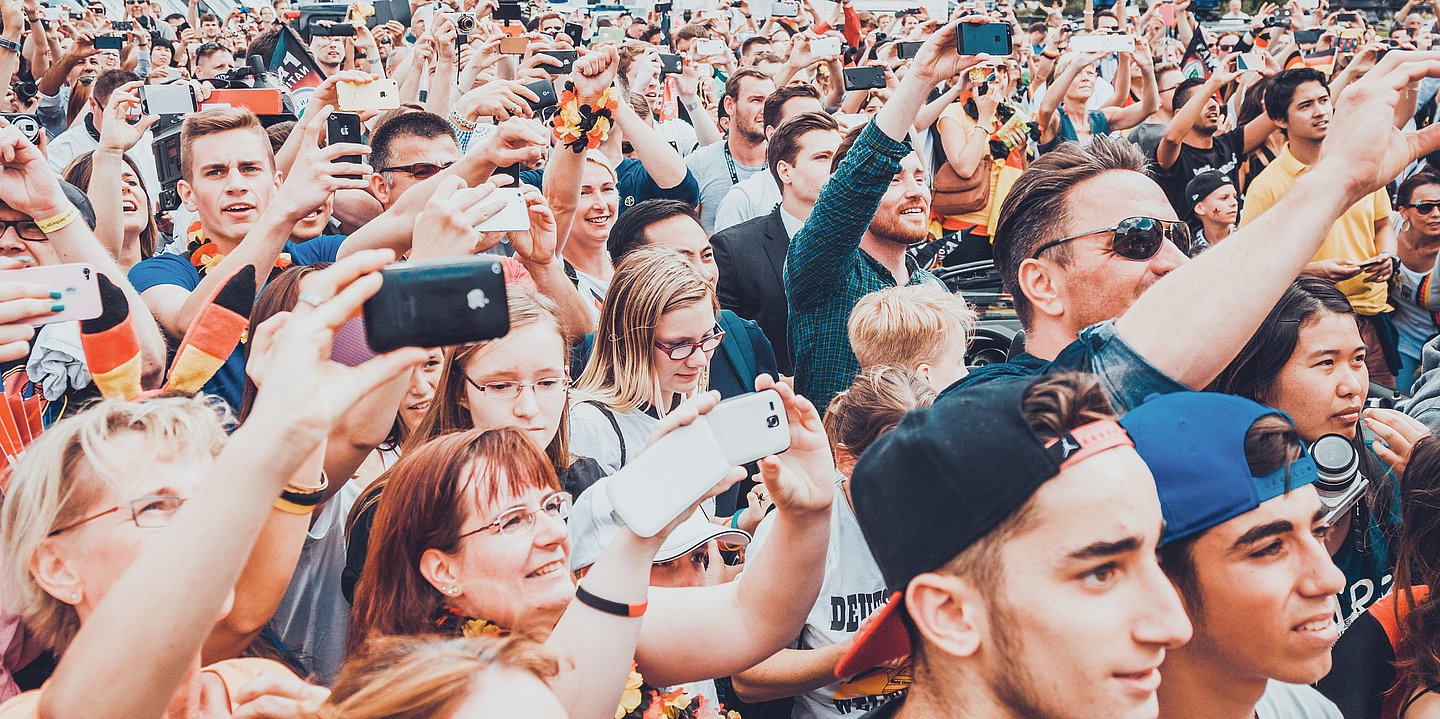 Foto: Eine Menschenmenge mit Deutschlandfahnen und -schals reckt die Hände in die Höhe und jubelt.
