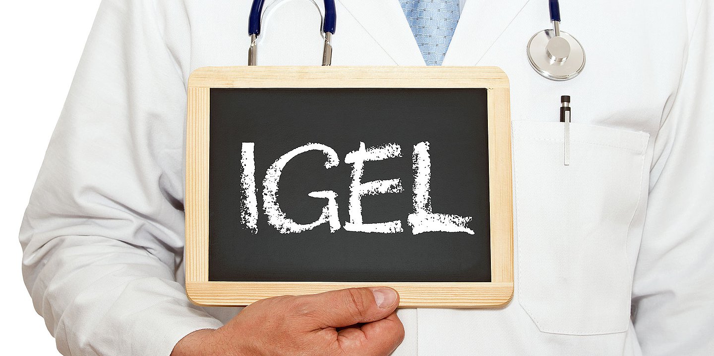 Foto: Ein Mediziner im weißen Kittel, von dem nur der Oberkörper zu sehen ist, hält eine kleine Tafel in der Hand, auf der "IGEL" steht.
