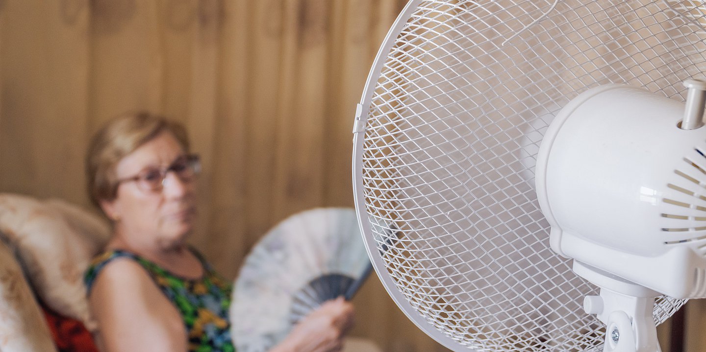 Foto: Frau sitzt mit einem Fächer vor einem Ventilator