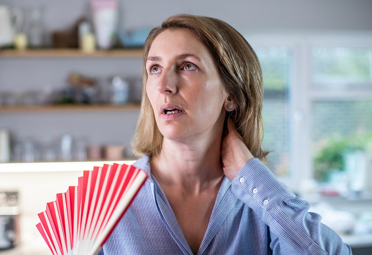 Eine Frau wedelt sich mit einem Fächer in der Hand Luft ins Gesicht.