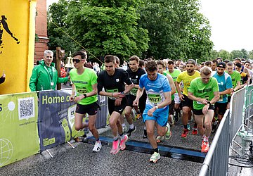 AOK-Business.Run Kiel 2024 Foto zeigt den Start des AOK-Business.Run Kiel 2024, der mit einer großen Glocke eingeläutet wird, die am linken Bildrand beim Torbogen des Starts zu sehen ist. Das Läuferwelt hat sich gerade in Bewegung gesetzt.
