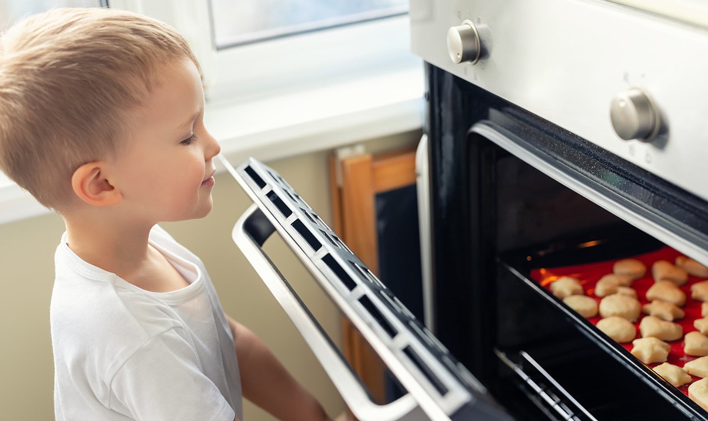 Das Foto zeigt einen kleinen Jungen, der die Backofentür öffnet, um sich die gebackenen Plätzchen anzuschauen.