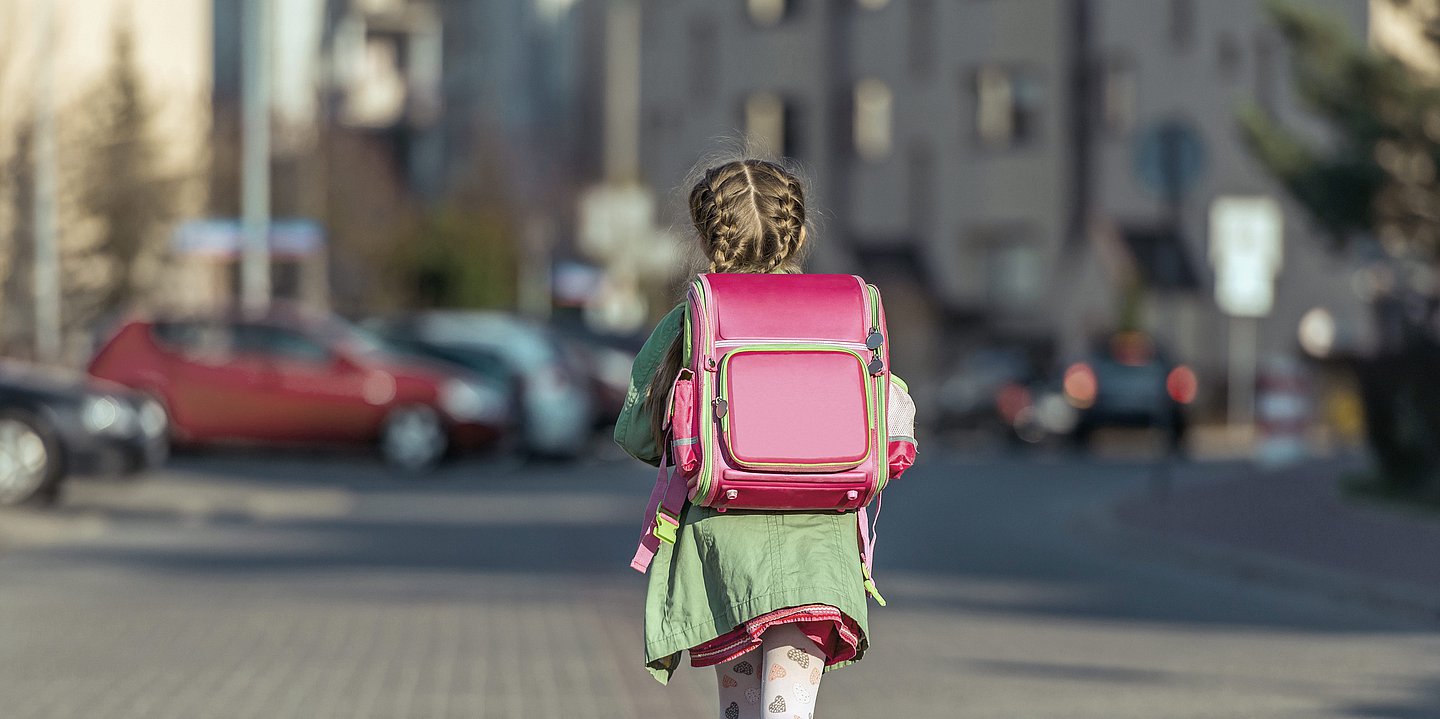 Ein Mädchen mit Schulranzen läuft durch die Straße.