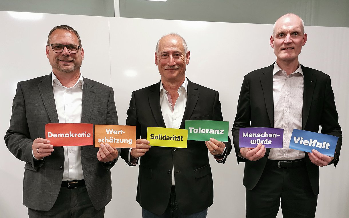 Luigi Colosi, Alexander Schmid und Jörg Schmautz halten Schilder hoch, auf denen mehrere ethische Werte zu lesen sind.