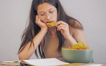 Emotionales Essen Foto: Frau sitzt am Tisch und isst Chips.