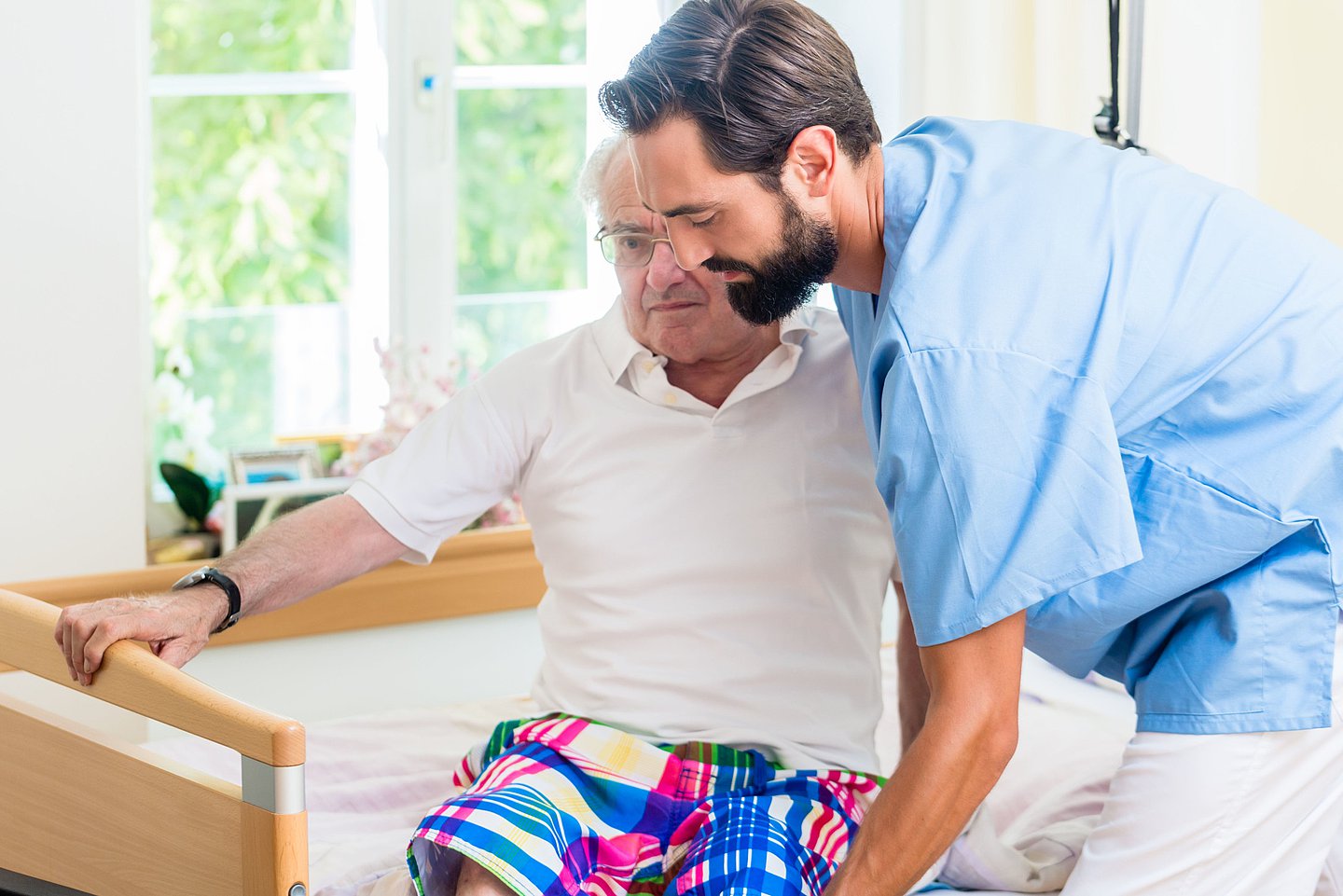 Das Foto zeigt einen Pfleger im Pflegeheim, der einem Pflegebedürftigen aus dem Bett hilft.