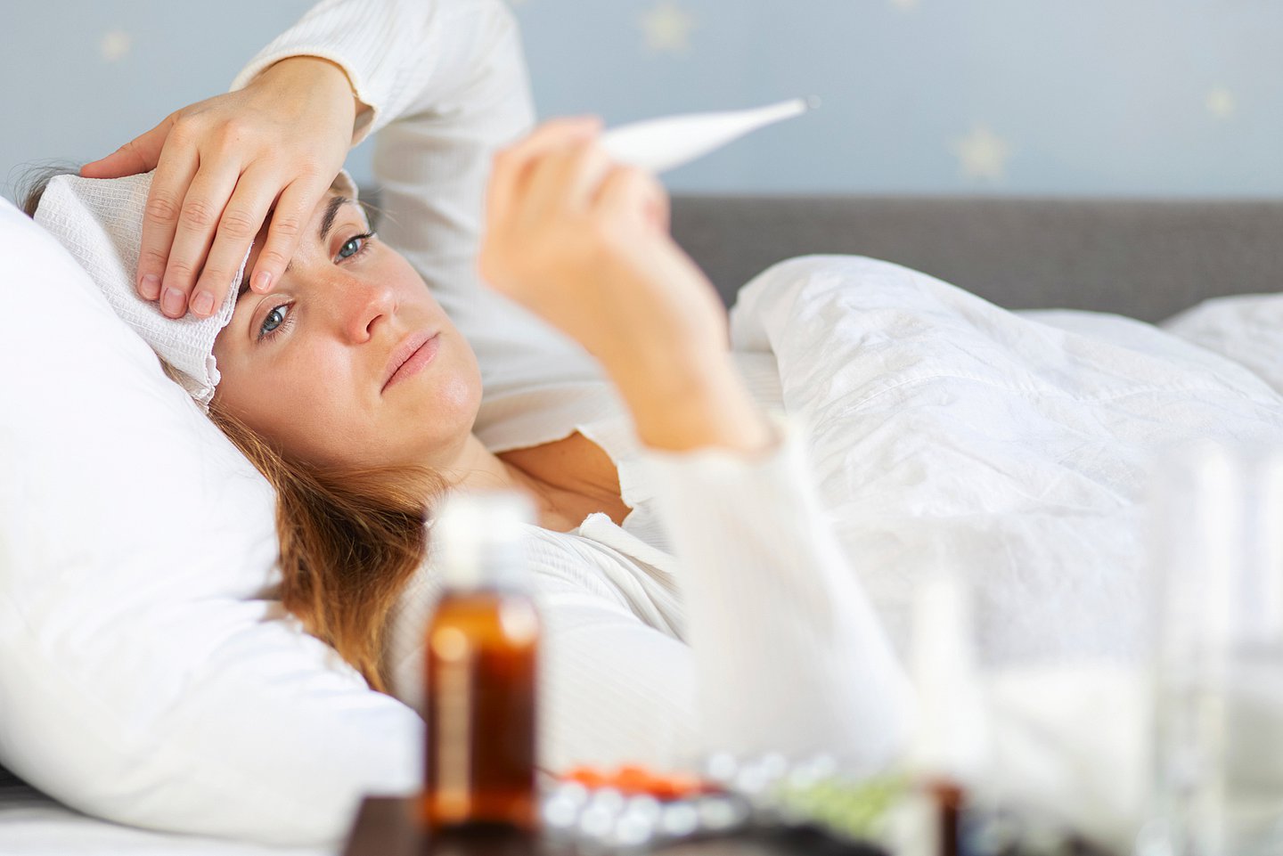 Das Foto zeigt eine Frau im Bett, die ein Fieberthermometer vor sich abliest.