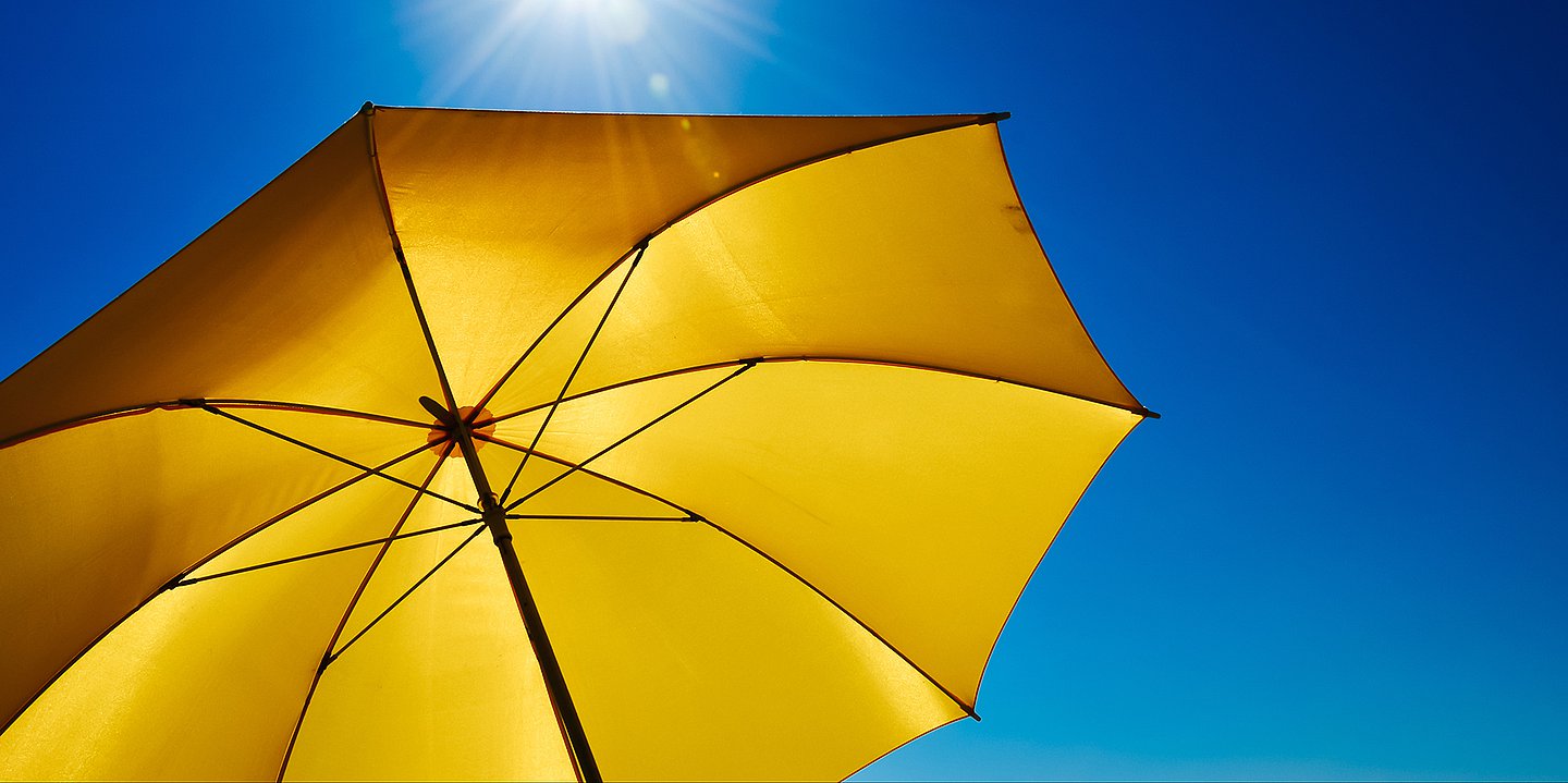 Foto: Ein aufgespannter gelber Schirm steht unter einem blauen Himmel.