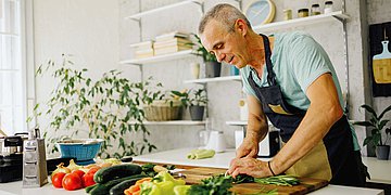 Gesunde Ernährung Ein Mann steht in der Küche und schneidet Gemüse.