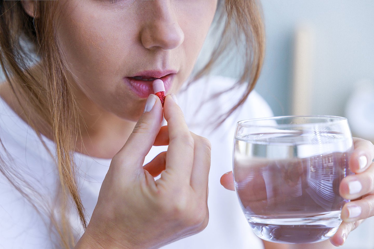 Foto: Eine Frau führt eine Tablette zum Mund und hält ein Glas Wasser in der Hand.