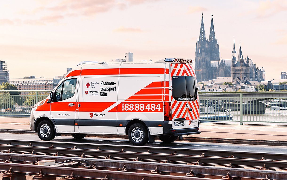 Foto eines Krankenwagens, der vor einer Stadtsilhouette über eine Brücke fährt