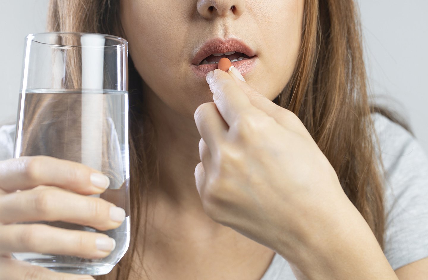 Eine Frau in Nahaufnahme steckt sich eine Tablette in den Mund und hält ein Glas Wasser in der Hand.