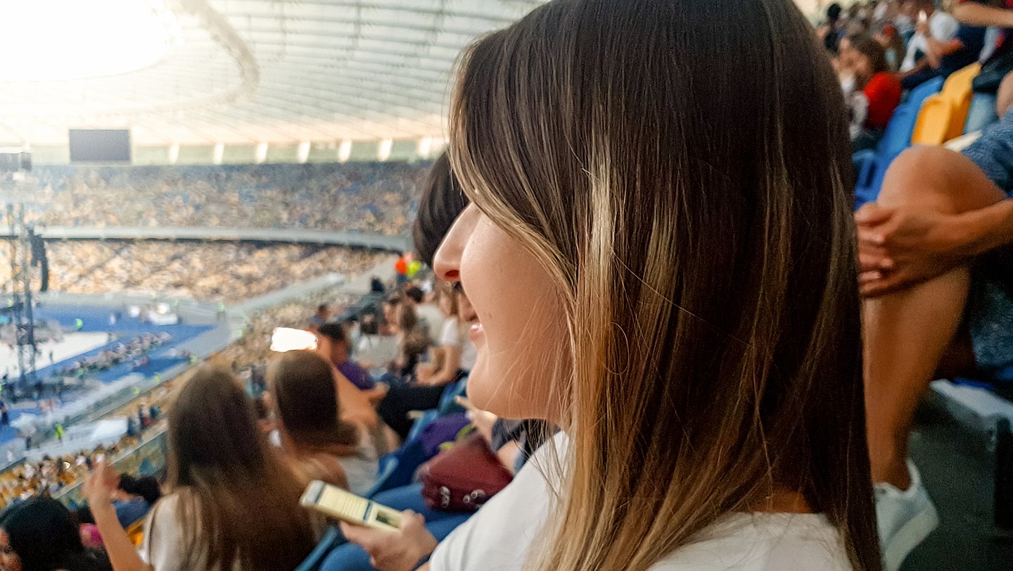 Foto zeigt im Vordergrund das Gesicht einer Besucherin, die im Fußball-Stadion ein Event verfolgt.