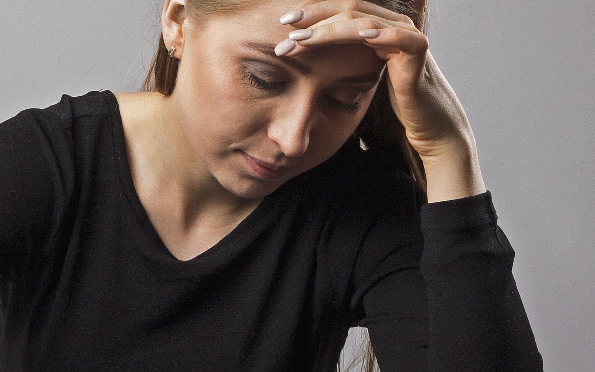 Eine Frau sitzt an einem Tisch. Sie schaut betroffen nach unten und stützt ihren Kopf mit der linken Hand.