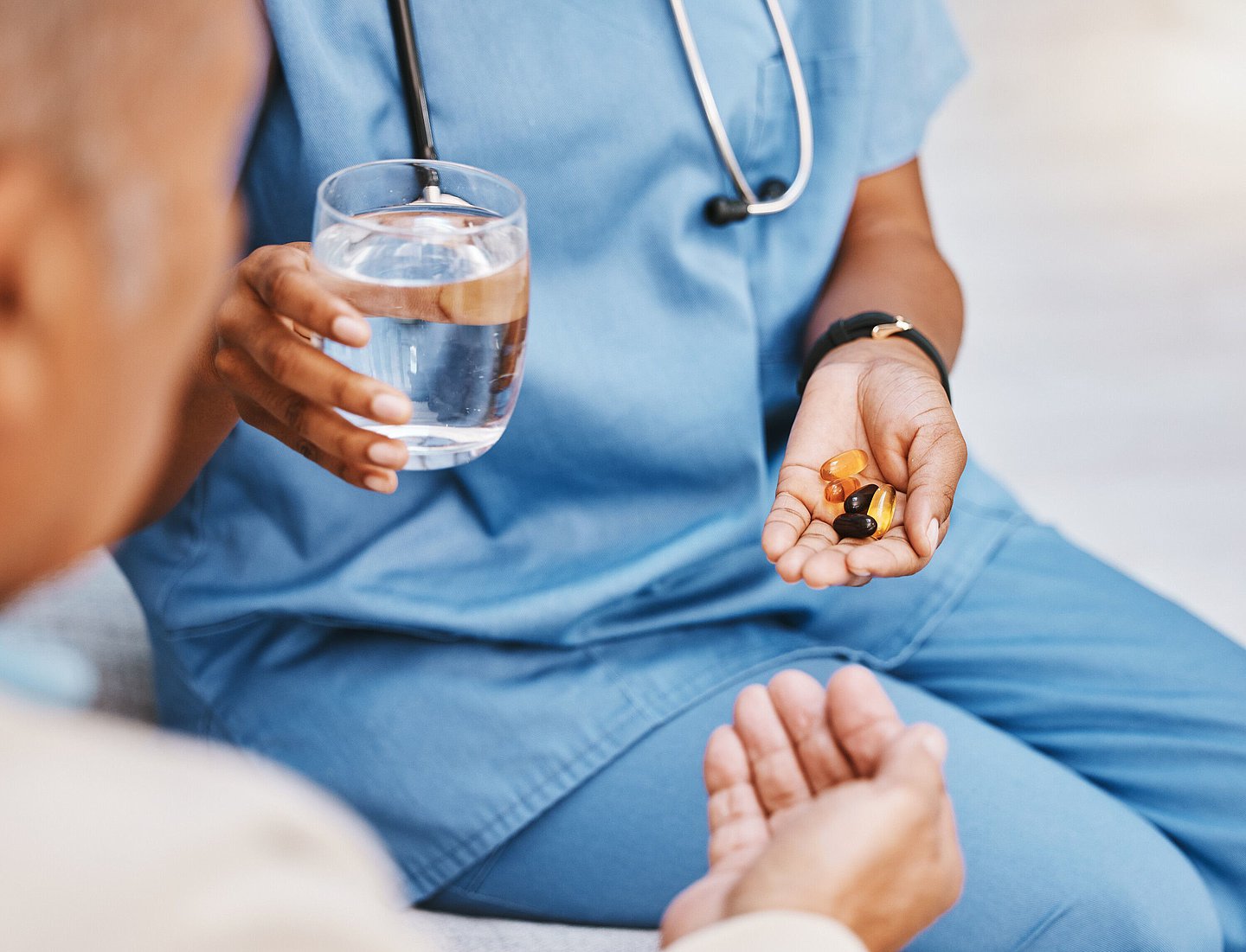 Foto einer Pflegekraft, die einem Patienten ein Glas Wasser und verschiedene Tabletten reicht