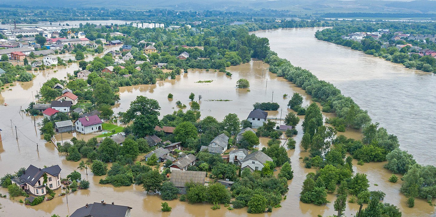 Ein Fluß ist über seine Ufer getreten und hat große Teile der Landschaft und einer Ortschaft meterhoch unter Wasser gesetzt.