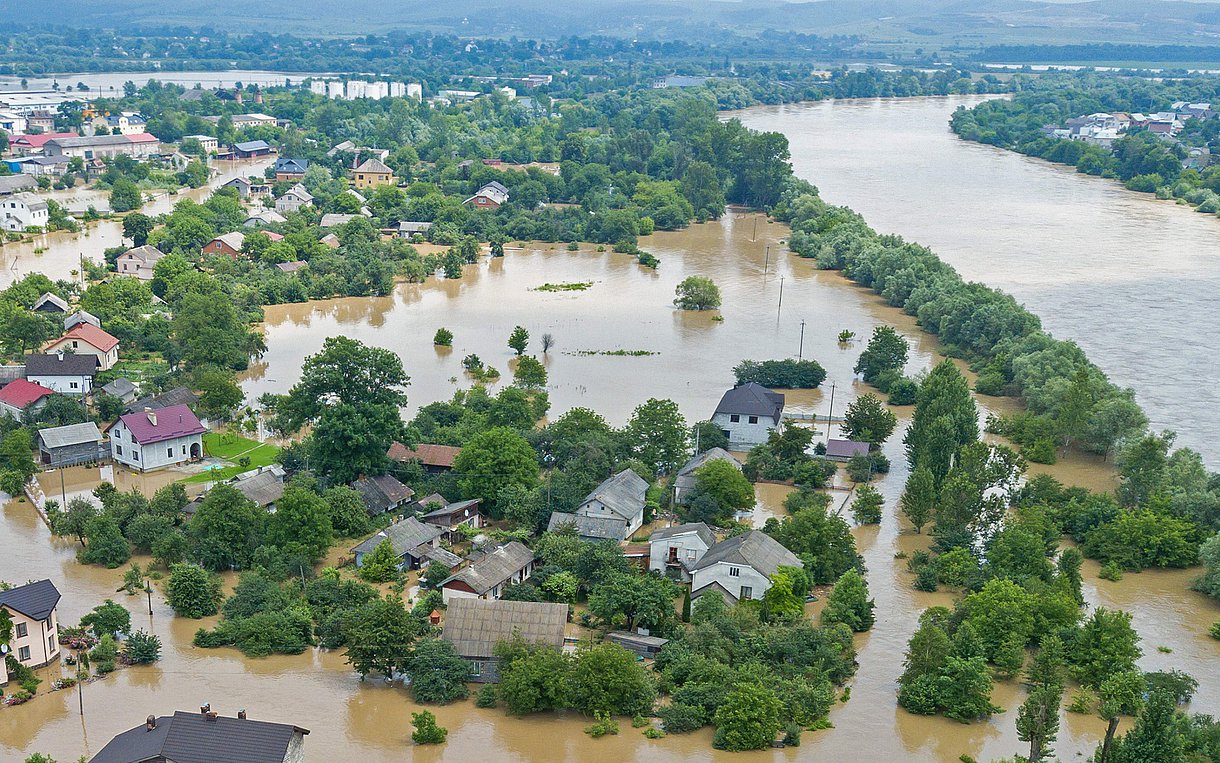 Ein Fluß ist über seine Ufer getreten und hat große Teile der Landschaft und einer Ortschaft meterhoch unter Wasser gesetzt.