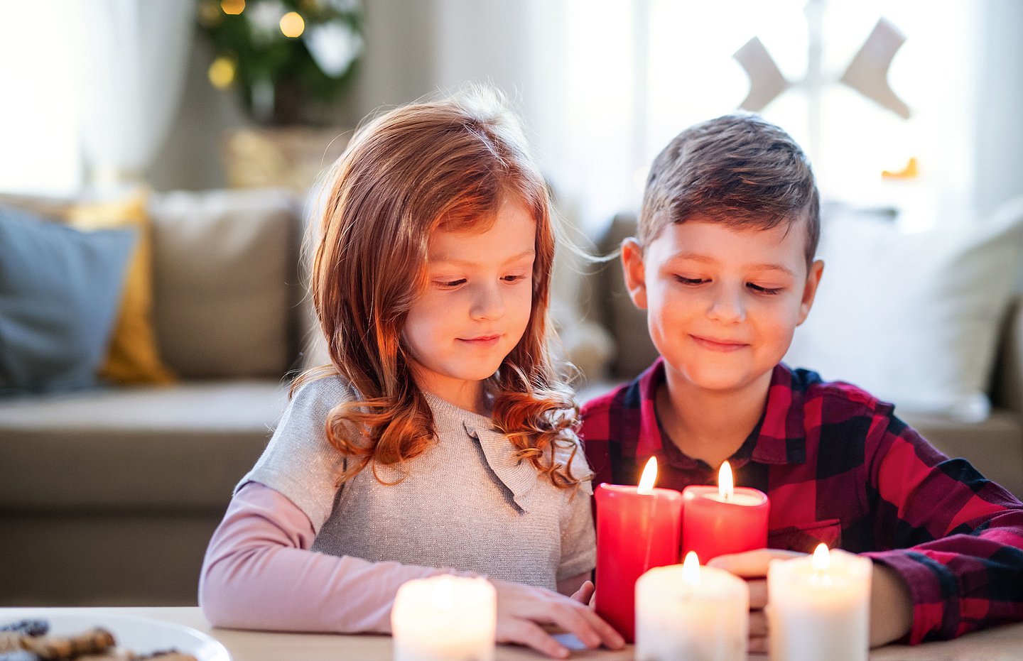 Das Foto zeigt ein Mädchen und einen Jungen, die sich brennende Kerzen anschauen.