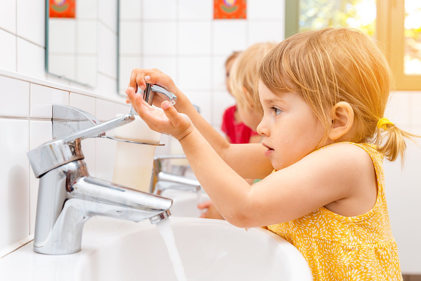 Kleine Kinder stehen im Waschraum einer KiTa und waschen sich die Hände.