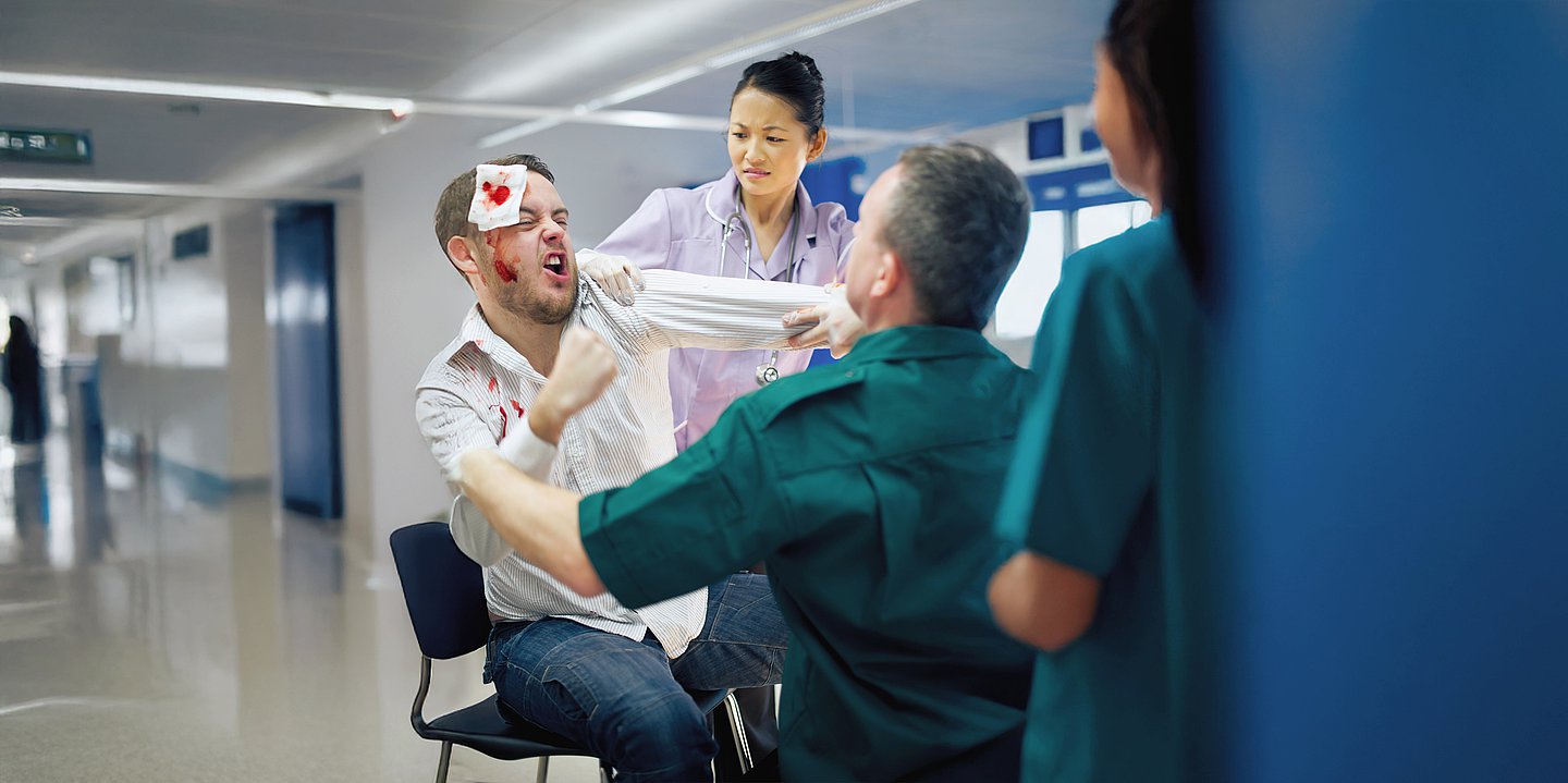 Foto: Ein Patient mit blutigem Gesicht und Verbänden geht auf Klinikpersonal los.