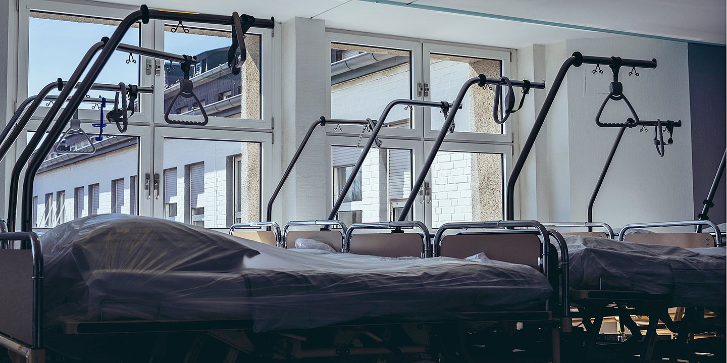Blick auf leere Klinikbetten vor einem Fenster in einem Krankenhauszimmer