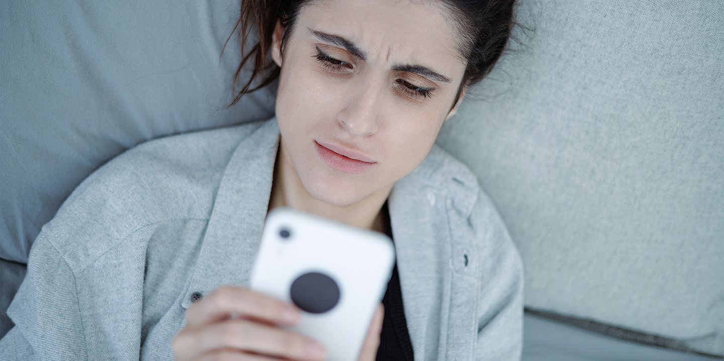 Foto einer Frau, die auf einem Sofa liegt und angestrengt in ihr Handy blickt