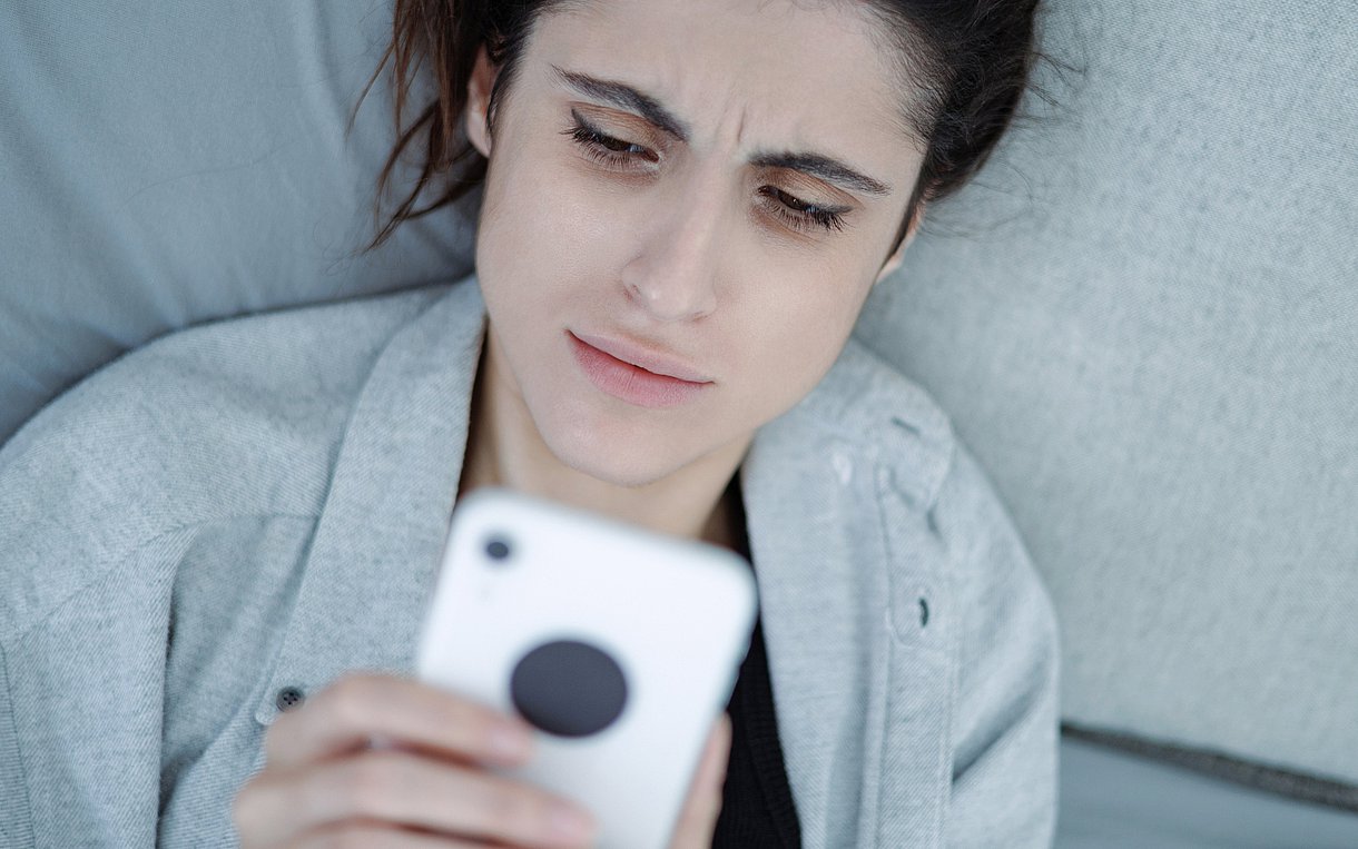 Foto einer Frau, die auf einem Sofa liegt und angestrengt in ihr Handy blickt