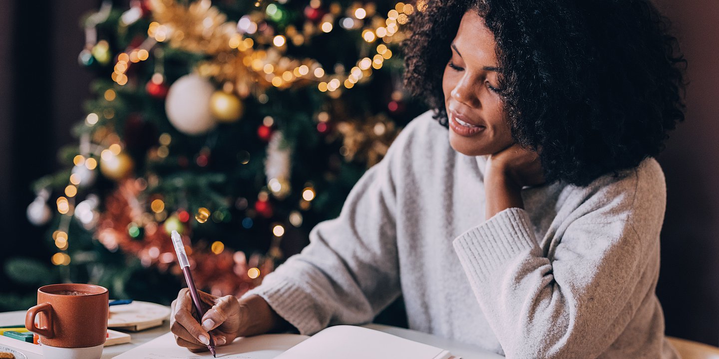 Eine Frau schreibt in weihnachtlicher Atmosphäre in einem Notizbuch.