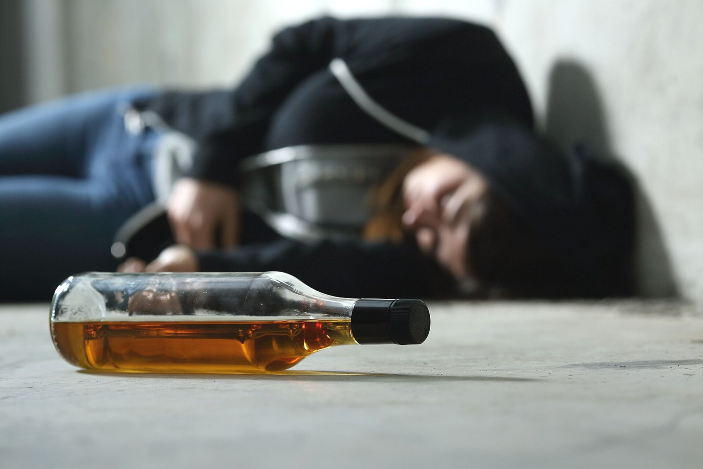 Eine Jugendliche liegt schlafend auf dem Boden neben einer Flasche Alkohol.