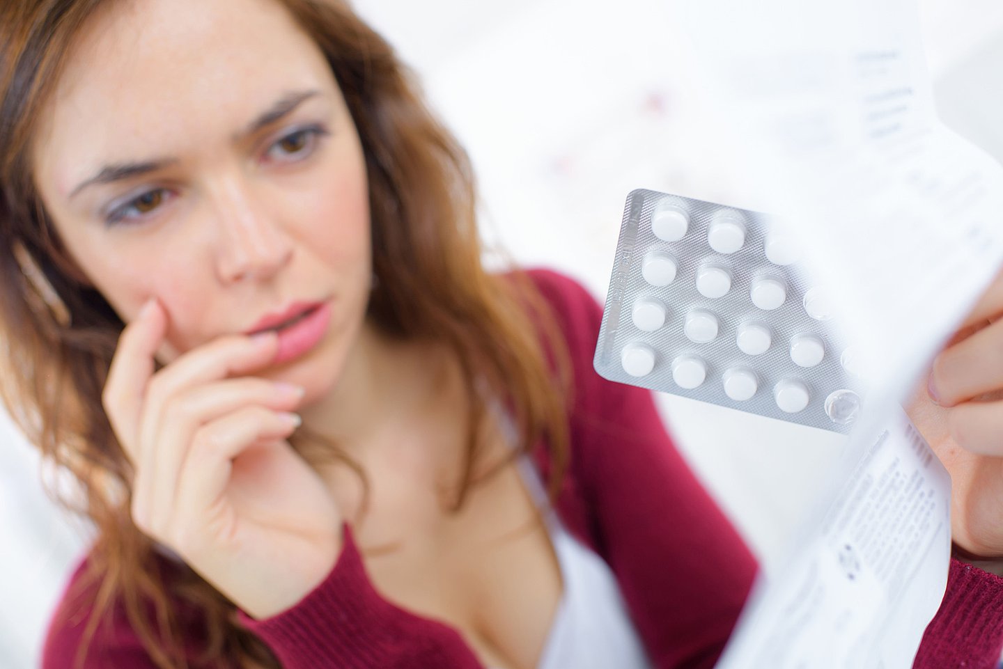 Frau hat einen Blister mit Tabletten in der Hand sowie den Beipackzettel, den sie durchliest.