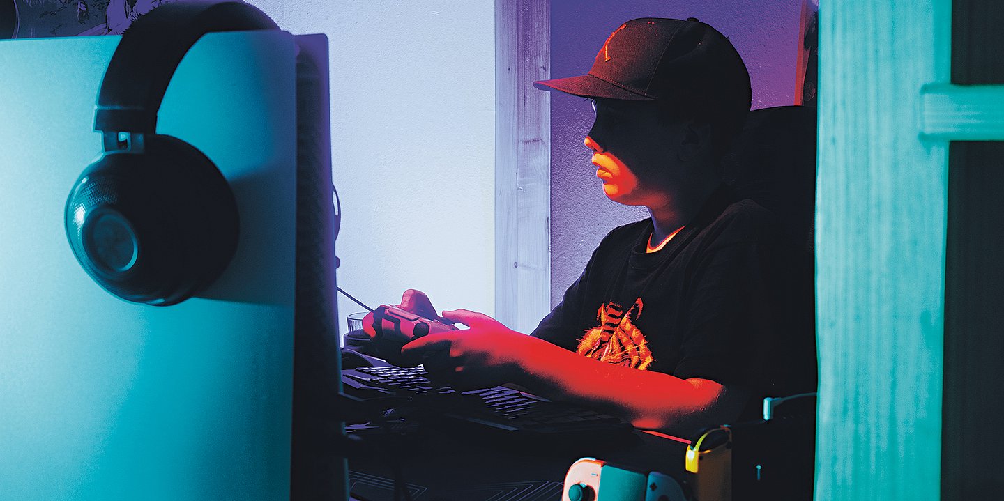 Foto eines jungen, der in einem düsteren Zimmer vor einem großen Bildschirm sitzt und zockt