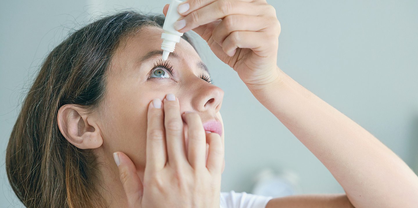 Foto: Eine junge Frau tropft sich Augentropfen in ein Auge.