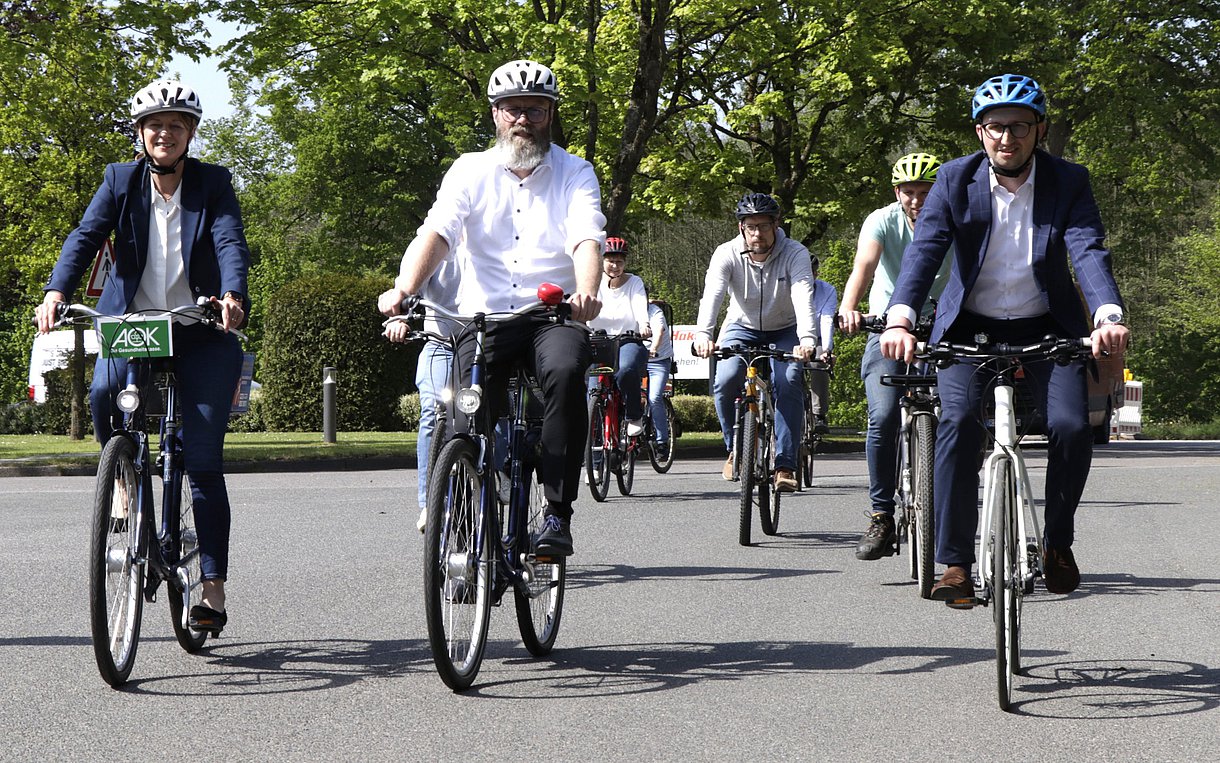 Foto zeigt eine Gruppe Menschen, die mit dem Fahrrad fahren. Vorneweg die AOK-Landesdirektorin Iris Kröner, Landes-Verkehrsminister Claus Ruhe Madsen und Hako-Geschäftsführer Blache. Es folgen dahinter weitere Mitarbeiter der Firma Hako.