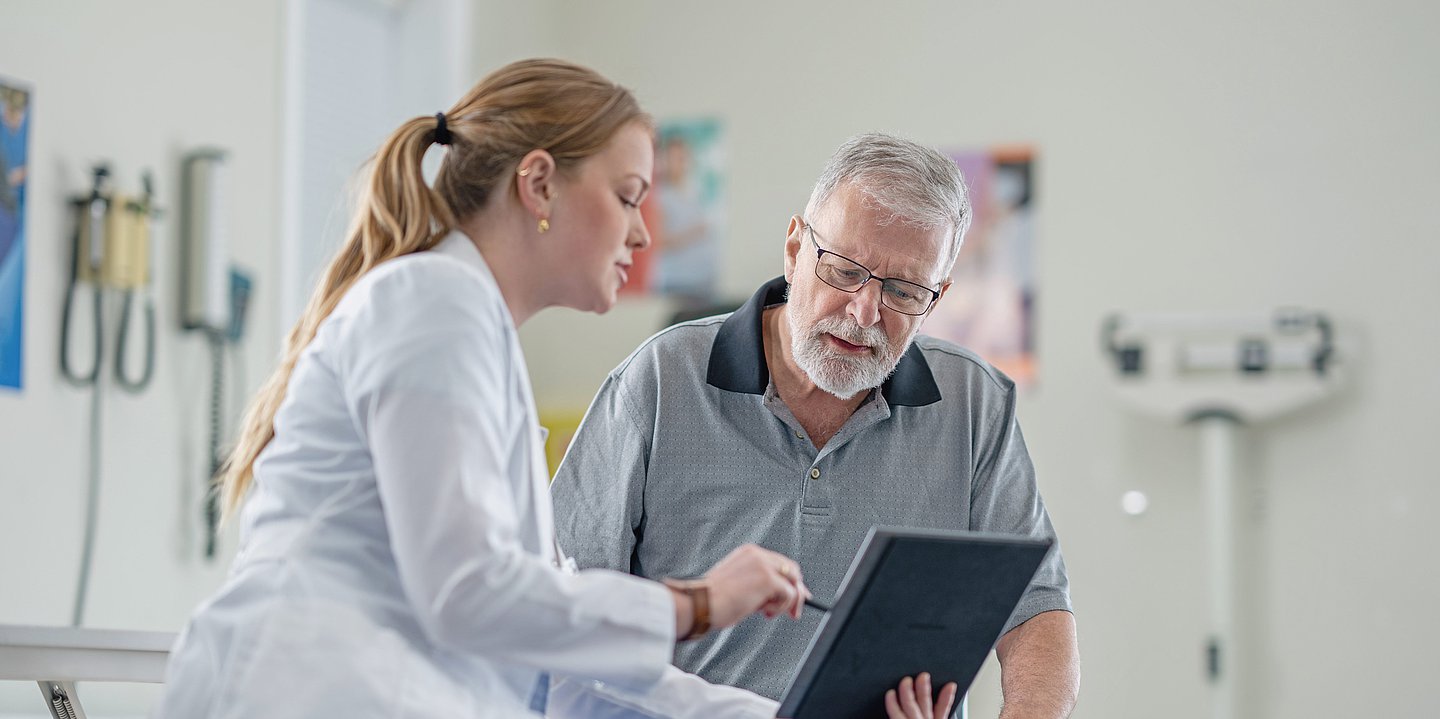 Eine medizinische Fachkraft berät einen älteren Patienten mit Hilfe eines Tablets.