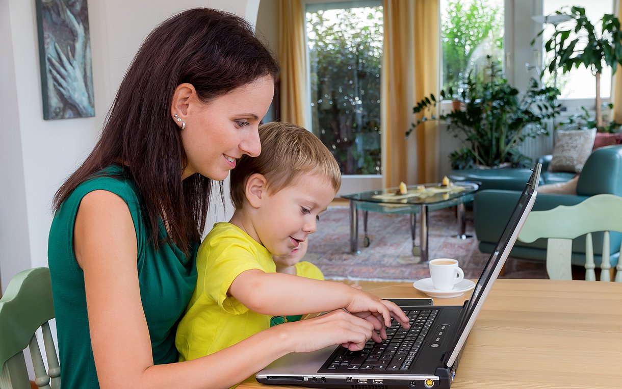 Eine junge Mutter sitzt mit ihrem Kind an einem Laptop.