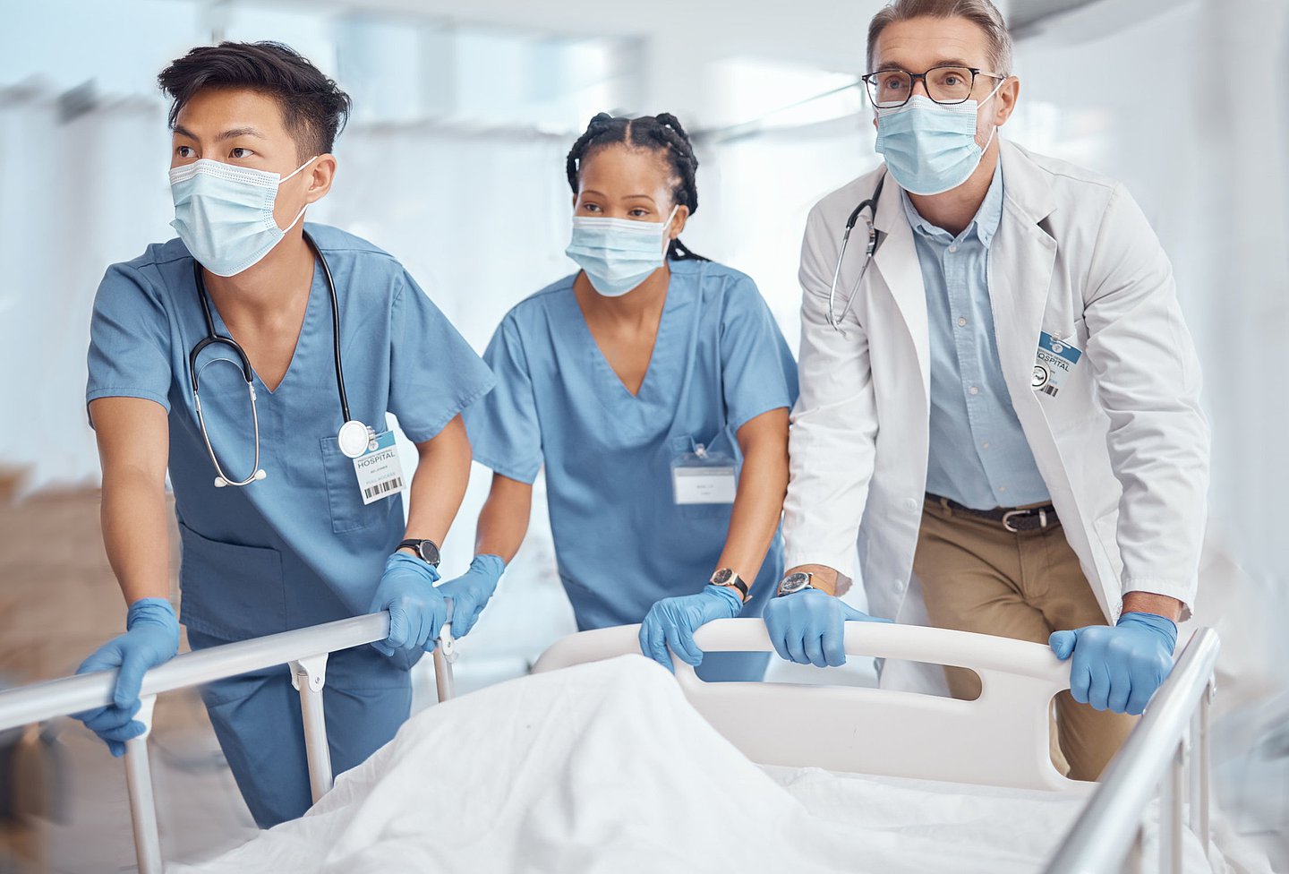 Foto von einem Arzt und Pflegern im Krankenhaus, die in Eile ein Krankenhausbett schieben.