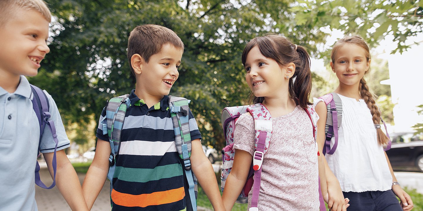 Vier Schulkinder, die sich an den Händen halten, mit fröhlichen Gesichtern