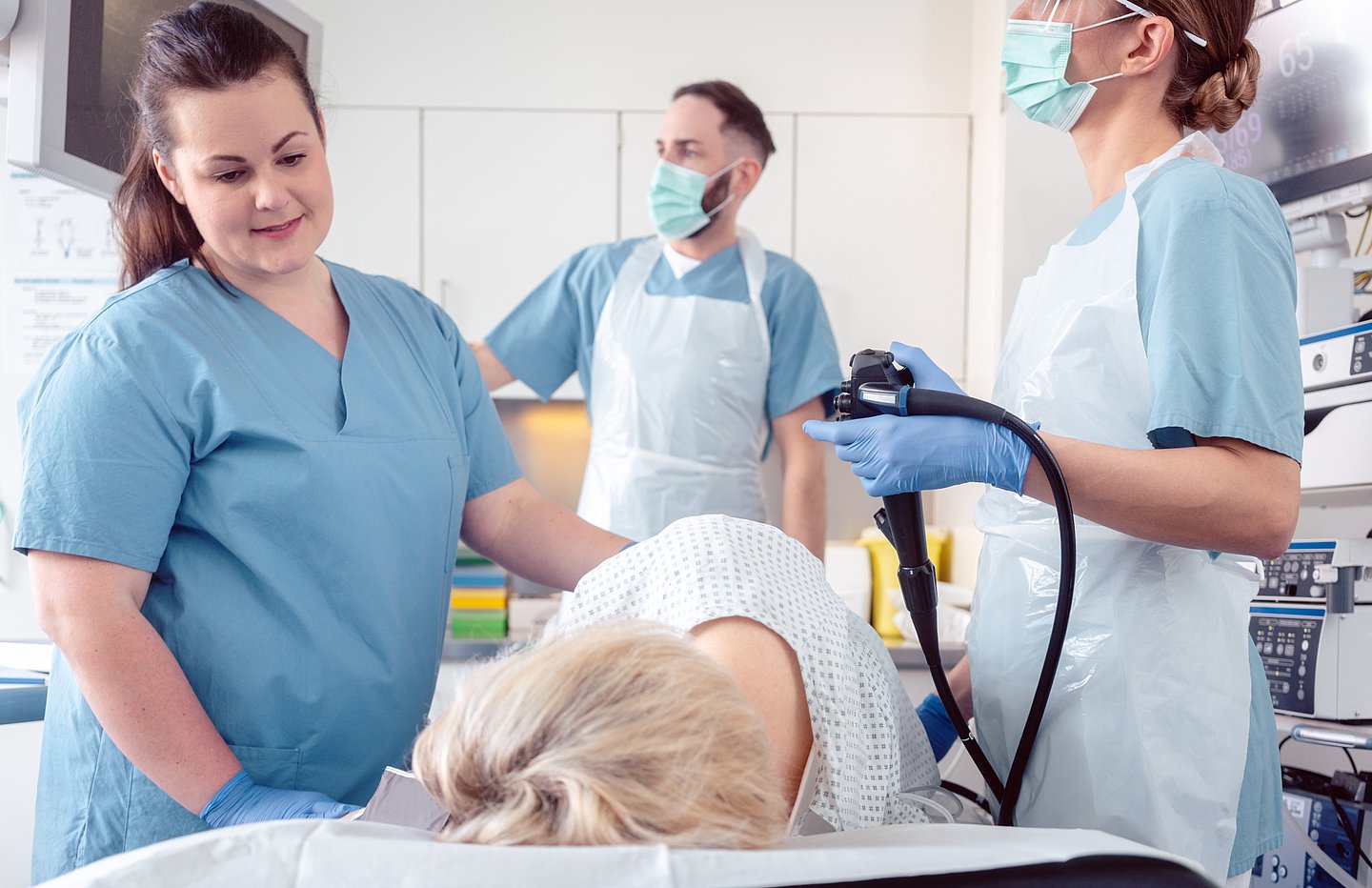 Ein Ärzteteam und Krankenpfleger führen im Krankenhaus eine Koloskopie an einer Patientin durch. Der Arzt verfolgt die Koloskopie auf dem Bildschirm. 